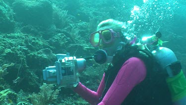 Scuba diver in a pink wetsuit taking photos on a reef