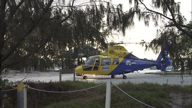 Yellow rescue helicopter on a beach with rotors spinning