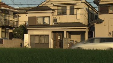 Car and a cyclist passing by a beige house