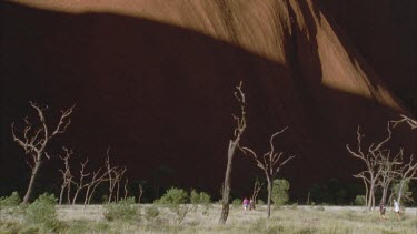 Uluru rock in background with shadow cast and people walk at base