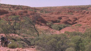 pan from people walking down natural rock steps of Kings Canyon to reveal the vast mounds of horizontal striated rock mounds similar to Kimberley