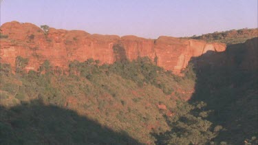 Time lapse of shadow moving across vegetated gorge with red rock cliffs either side