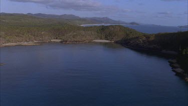 aerials of Whitsunday island pass low over water then forest onto Whitehaven beach