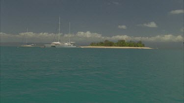 sailing boats anchors on idyllic blue reef waters next to island