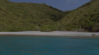 tracking along island shore with beautiful white sand beach and hoop pines on shore and Eucalypt covered hills behind