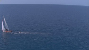 track over blue waters and yacht under sail trailing a dingy