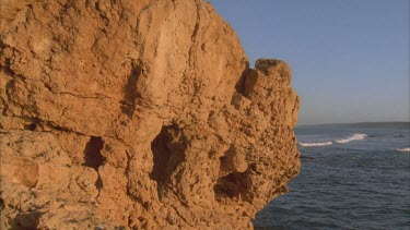 rich orange rock outcrop probably limestone with waves behind pan to show land on other side of the bay