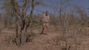 scientist Andrew Parker walking through bush tracking stops and crouches to inspect fresh spoor signs