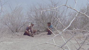 bushman woman and little boy picking out beetle larvae for poison arrow , little boy runs out of shot , women walks out