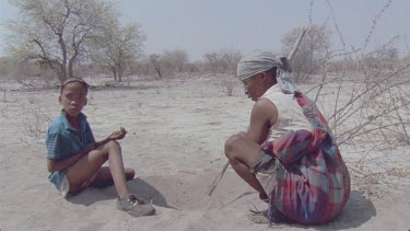 bushman woman and little boy picking out beetle larvae for poison arrow , little boy runs out and woman follows