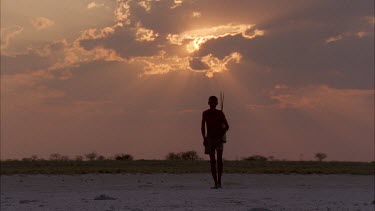 bushman silhouette walking away from camera and into sunburst sunset with bow and arrows over shoulder , very nice shot , a classic , very steady , various takes