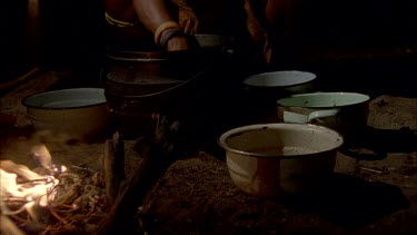 Bushman camp , with campfire , woman sitting beside fire , smoking a pipe , stirring cooking pot