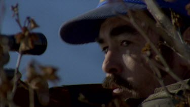 Inuit hunter's head through tree as he aims and fires his gun