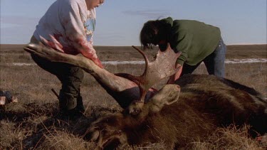 Two Inuit men cutting off dead moose leg