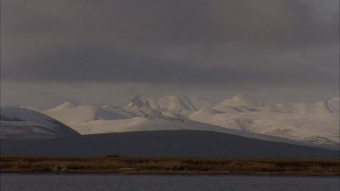 white clouds blowing over low lying snow covered hill