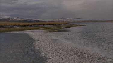 frozen waters edge of a lake, pan up to tundra landscape.