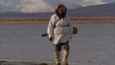 Inuit man walking along frozen edge of the lake