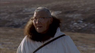 Inuit trackers walk towards camera with vast, barren tundra landscape in background