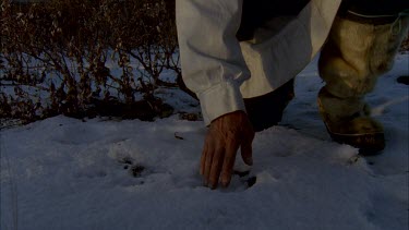 Inuit trackers face examining moose track. He looks up, stands up and walks out of frame.