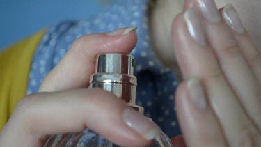 Young lady sprays perfumes on her hand first and than applies it to her neck.