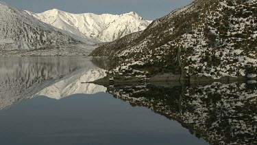 White snow peak mountains reflected in clear still water of lake.
