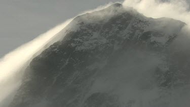 Anabatic wind blows strongly up steep slope of mountain. Shot shows cloud, mist travelling up the mountain. The clouds are brightly illuminated by the sunshine behind. Shows how wild weather can occur...