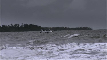 Boat out at sea with very rough stormy water. Boat tethered or anchored in shallow waters.