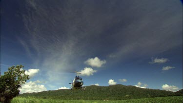 Low angle shot of helicopter approaching and flying over camera. Deep blue sky with clouds above.