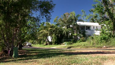 Cassowary in suburban landscape, walks across road. There is a white weatherboard house in the background. Mission Beach, tropical north Queensland.