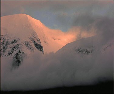 Clouds hanging over mountain peaks, weak pinkish lighting