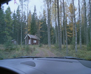 Car drives rural forested Scandinavian landscape. Farmhouse