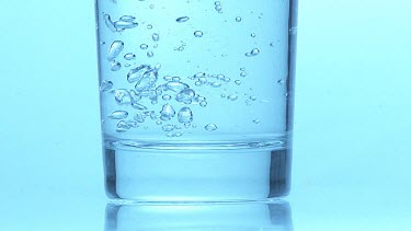 Glass of Sparkling Water against Blue Background, Slow Motion