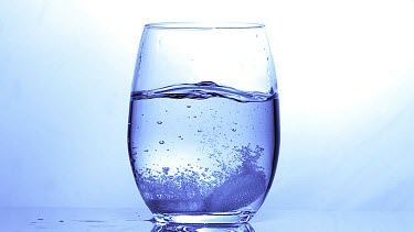 Tablets Falling into a Glass of Water against Blue Background, Slow Motion