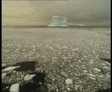 Track over cracked and melted ice floe with iceberg in background.