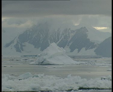 Iceberg with snow covered rocky mountain in background