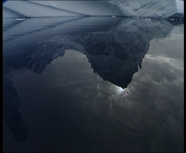 Sun shining through clouds and tip of iceberg reflected in still water