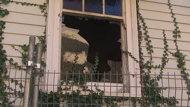 Broken glass window in shingled wood house.