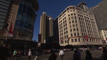 Busy central Sydney intersection with lots of pedestrians crossing road. Traffic (cars) stopped at traffic light. Wide Shot. (Town Hall).