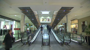 People in shopping mall, shopping centre going up and down escalators