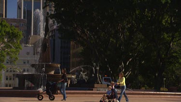 Tilt Up Sydney Centrepoint Tower from Hyde Park. Two people in shot, mother's pushing babies in strollers.