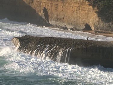 One man standing on eroded rock, waves crashing in front of him