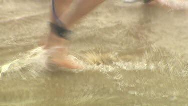 Feet walking across beach, the waves lap over gently