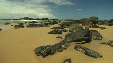 Black rocks on beach, could be volcanic origin.