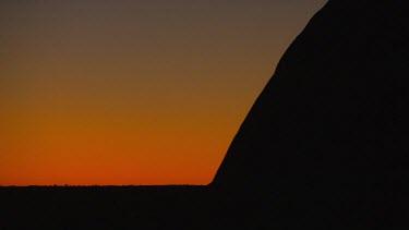 Sunset Uluru, the curve of the rock in silhouette against a red sky