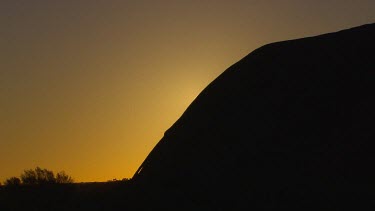 Sunrise. Sun rising behind curve of rock of Uluru.