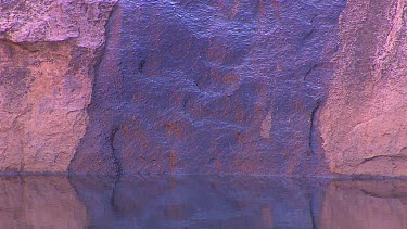 Water pool at base of rock. Wet rock is black. Water flowing in desert.