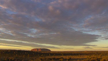 Typical iconic wide shot of Uluru time lapse clouds moving across sky.