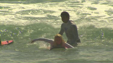 Young woman learning to surf falls off surfboard