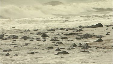 Waves crash over black stones on beach