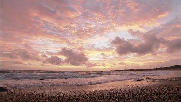 Beach at sunset with pinkish hues in sky. Clouds.
